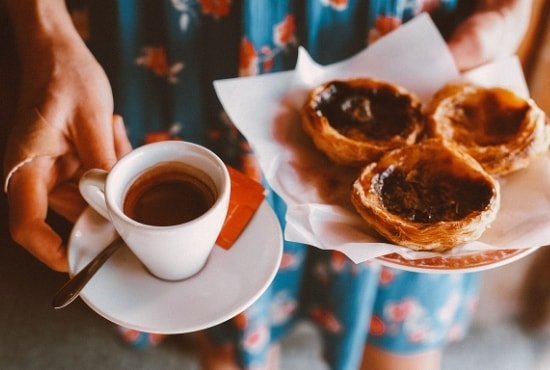 Women holding a plate with three custard tarts in one hand, and in the other a cup of coffee