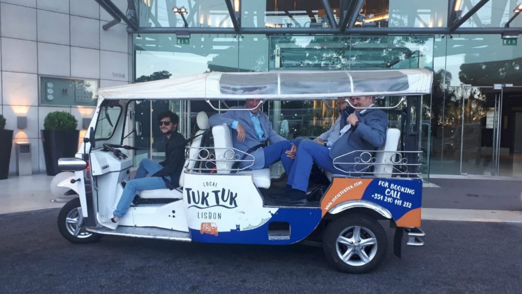 Three business men inside a tuk tuk outside an hotel entrance