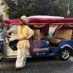 Person wearing arabic style clothes stading next to a tuk tuk decorated for the release of the game Uncharted: The Lost Legacy