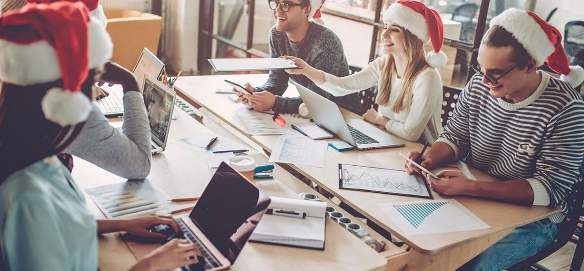 Group of people gathered around a table working while hearing Christmas hats